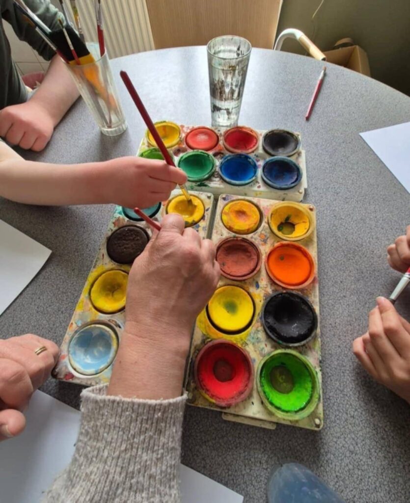 Barn och en vuxen som doppar penslar i målarfärg